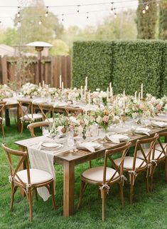 an outdoor dinner table set up with white and pink flowers, greenery and candles