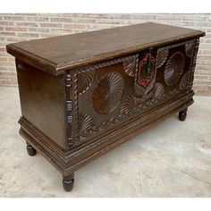 an old wooden chest with ornate carvings on the front and sides, sitting against a brick wall