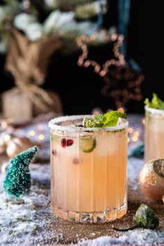 two cocktails sitting on top of a table covered in snow next to christmas decorations