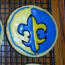 three decorated cookies with blue and yellow icing on a cooling rack, one has the letter e