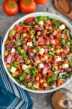 a salad in a white bowl with tomatoes, olives and ham on the side