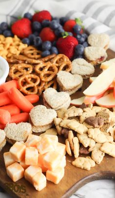 a wooden cutting board topped with cheese, crackers, fruit and pretzels