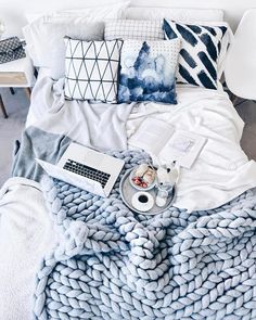 a bed covered in blankets and pillows next to a laptop computer on top of a table