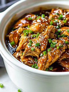 a white bowl filled with chicken covered in sauce and green onions on top of it