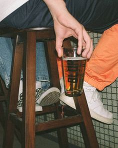 a person sitting on a stool with a drink in front of their feet and legs