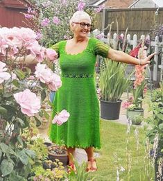 an older woman in a green dress standing next to pink flowers and potted plants