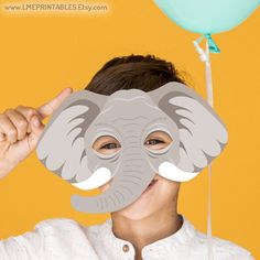 an elephant mask is being held up by a woman's face with balloons in the background