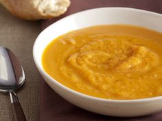 a bowl of carrot soup with a spoon next to it on a brown table cloth