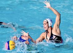 two women are playing water polo in the swimming pool while one woman is trying to block the ball