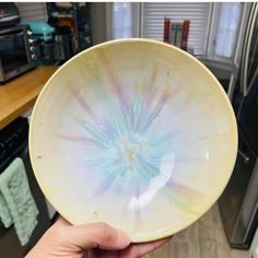 a hand holding a white bowl with blue and green designs on it in front of a kitchen counter