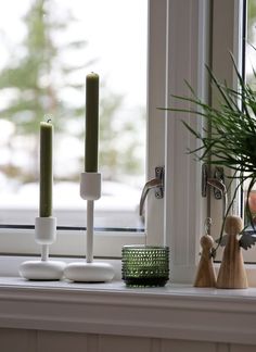 two candles are sitting on a window sill next to a potted plant and candle holders