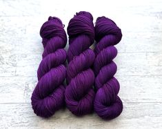 three skeins of purple yarn sitting on top of a white tile floor next to each other