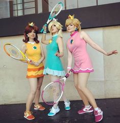 three women dressed in costumes holding tennis racquets and posing for the camera