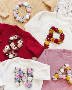 four sweaters with flowers on them are laying next to each other and one is wearing a flower brooch