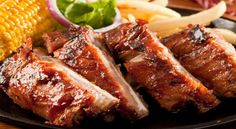 barbecue ribs, corn on the cob and coleslaw are served on a black plate