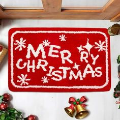 a merry christmas door mat surrounded by holiday decorations and bells on top of a table