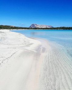 an empty beach with blue water and mountains in the background