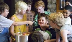 a group of young people standing around each other in front of a metal pan with food