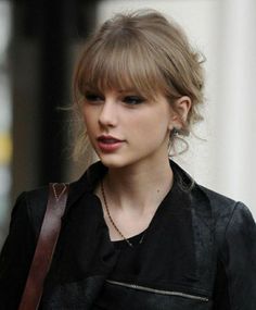 taylor swift is walking down the street with her hair in a bun and wearing a leather jacket