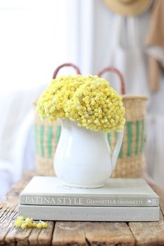 a white vase filled with yellow flowers sitting on top of a table next to a book