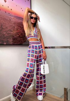 a woman is standing in front of a painting and holding a white handbag while wearing colorful clothing