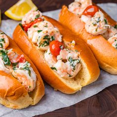 three lobster sandwiches on bread with lemon wedges and garnished with fresh herbs