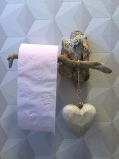 a toilet paper roll hanging on a wall next to a heart shaped rock and driftwood