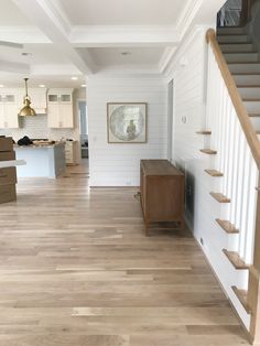 an empty living room with stairs leading up to the second floor and kitchen in the background