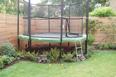 a trampoline in the middle of a garden with grass and bushes around it