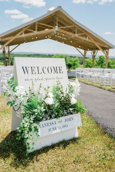 a welcome sign with flowers and greenery in front of an outdoor wedding ceremony venue