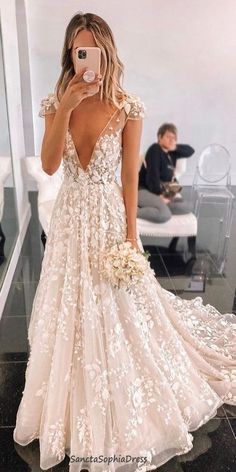 a woman taking a selfie while wearing a wedding dress with floral appliques