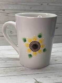 a white coffee cup with yellow flowers painted on it's side sitting on a wooden table