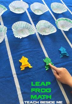 a person is making paper fish on a blue tablecloth with white stripes and green letters