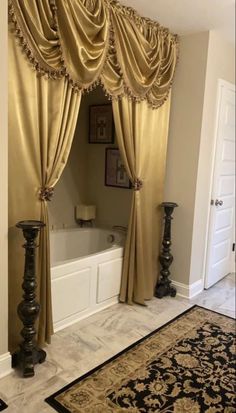 a bath tub sitting next to a window covered in gold drapes and draperies