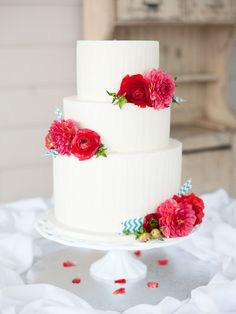 a three tiered white cake with red flowers on top