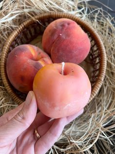 a hand is holding a peach in a basket with straw on the floor next to it