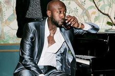 a man in a suit sitting at a piano drinking from a wine glass and looking off to the side