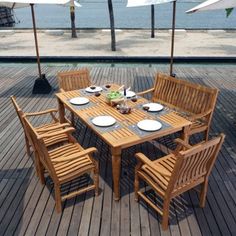 an outdoor dining table set with umbrellas and plates on the wooden deck overlooking the water