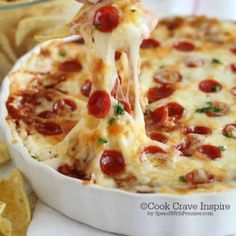 a person is dipping cheese into a dish with pepperoni and olives on top