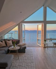 a living room filled with furniture next to an open window overlooking the ocean at sunset