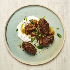 a plate topped with meat covered in sour cream and garnished with green herbs