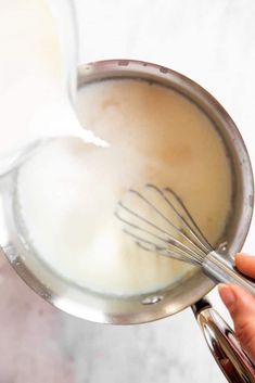 a hand holding a whisk in a glass bowl with milk and other ingredients