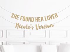 a white couch sitting next to a wall with a gold banner on it that says she found her lover nicole's version