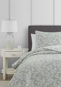 a bed with a white and green comforter on it next to a night stand