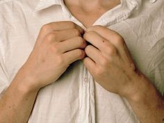 a man in white shirt tying his tie with both hands and wearing a button down collar