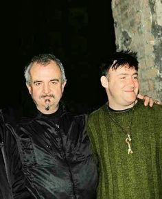 three men standing next to each other in front of a stone wall with a cross on it