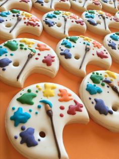 decorated cookies with paintbrushes on them sitting on an orange tablecloth covered in white icing