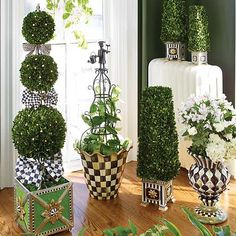 three vases filled with plants and flowers on top of a wooden floor next to a window