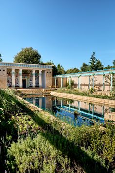 an outdoor swimming pool surrounded by greenery next to a building with columns on the side