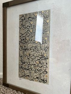 an arabic calligraphy is displayed in a frame on the floor next to a carpet